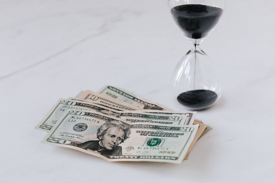 From above of transparent glass with black sand on white table and pile of paper money with image of president