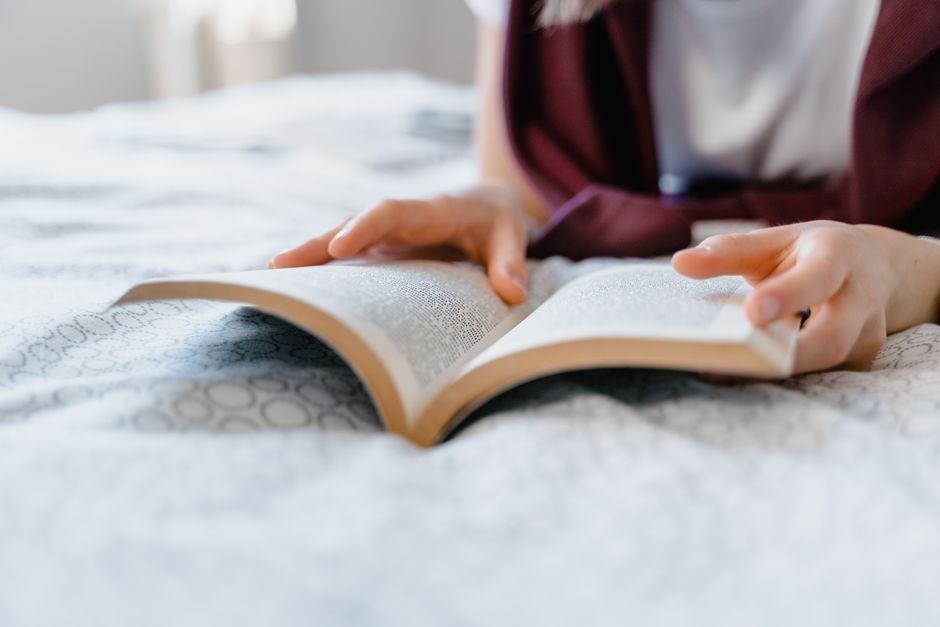 A person leisurely reading a book in bed, enjoying a peaceful indoor setting.